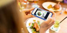 A woman photographing her food with a smartphone. She's going to make a social media post about her experience in the restaurant she's eating in
