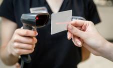 A person holding a laser scanner and scanning a loyalty card held by a customer.