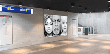 An empty metro station entrance. Side-by-side on the wall are three sleek screens showing an ad.