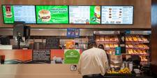 A man standing at a counter. Digital menu boards hang overhead