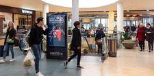 Multiple people walking past a digital screen. The screen is displaying an ad from the Pepsi Max programmatic campaign.