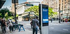 A man standing at a LinkNYC kiosk on a sunny day.