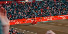 A soccer team celebrating by the sideline. Ads for Coca Cola are running on the digital displays that run along the field's perimeter